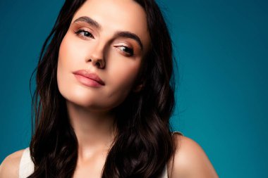 Çarpıcı genç bir kadın model, doğal güzelliği, taranmış saçlarıyla, değişken mavi arka planda, ışık saçan cazibe ve entelektüelliği sergiliyor..