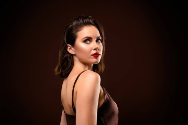 Kısa esmer saçlı bir kadının portresi, zarif bir kıyafet giyiyor, bir stüdyo ortamında kendine güvenerek poz veriyor, güzelliğini ve tarzını ön plana çıkarıyor..