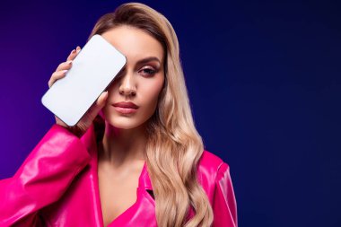 Çekici bir tarzı ve sarı saçları olan, menekşe arkaplanının önünde pembe bir trençkot giymiş güzel bir genç kadın..