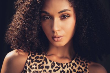 Dramatik ışıklandırması ve leopar desenli elbisesi olan genç bir kadının doğal cazibesini ve kendine güvenini vurgulayan yakın plan portresi..