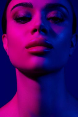 Genç bir kadının yüzü neon pembe ve mavi ışıkla aydınlanarak canlı ve şık bir etki yaratıyor..