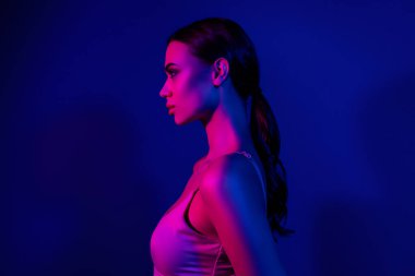 Neon mavisi ve pembe ışıklandırmayla yıkanmış genç bir esmer kadın profili, zarafeti vurguluyor, canlı moda, ve ultraviyole renk ayarında şık bir güzellik..