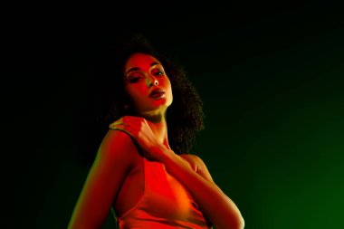 Renkli, parıltılı bir ışıkla poz veren zarif genç bir kadın. Gösterişli bir cazibe, moda ve şenlikli bir atmosferde kendine güven..