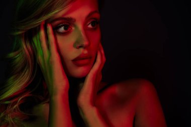 Sarışın, neon kırmızısı ve yeşil ışıkta yıkanmış, koyu bir arka plana karşı güzellik ve lüks saçan genç bir kadının büyüleyici görüntüsü..