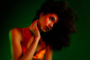 Çarpıcı kıvırcık saçlı, şık bir kokteyl elbisesi giyen, çarpıcı renkli ışıklandırmayla tasvir edilmiş zarif, güzel ve göz alıcı bir stüdyo ortamında.