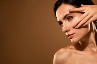 Açık bej bir arka planda zarifçe poz veren güzel, genç bir esmer kadın doğal güzellik ve cilt bakımını vurguluyor..