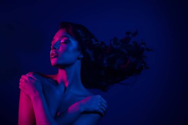 Kalın pembe ve mavi neon ışıkla aydınlatılmış şık bir kadın. Yaratıcı ışıklandırma düzeneği altında sofistike ve kendine güvenen biri..