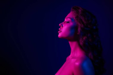 Canlı neon mavi ve pembe ışıkla aydınlatılmış, modern güzellik ve stili çağrıştıran genç ve çekici bir kadının büyüleyici bir profil çekimi..