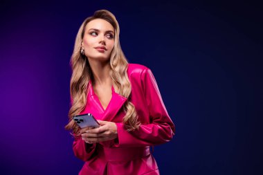 Zarif, pembe bir trençkot giymiş, elinde akıllı bir telefon tutan, canlı mor bir arka plana karşı poz veren, güzellik, sofistike ve çağdaş bir yaşam tarzı ifade eden zarif sarışın kadın..