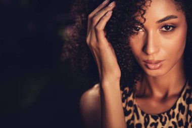 Yumuşak ışıklı kıvırcık saçlı çarpıcı bir genç kadının portresi. Görüntü onun zarif güzelliğini, modaya uygun tarzını ve doğal atmosferini vurguluyor..