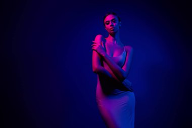 Göz kamaştırıcı bir kadın model zarif bir şekilde poz veriyor, neon pembe ve mavi ışıklarla kaplanmış, büyüleyici bir atmosferik ortamda lüks, güzellik ve gece hayatını çağrıştırıyor..