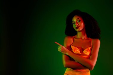 Zarif bir şekilde şık giyinmiş genç bir kadın yeşil bir arkaplan önünde poz veriyor. Kendine güveni ve güzelliği, cazibeyi, şık modayı, kutlama ve cazibe atmosferini temsil ediyor..