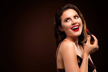 Canlı kırmızı ruj sürerken, güzel ve zarif bir şekilde gülümseyen çekici bir genç kadın. Karanlık bir arkaplanda, cazibeyi, stili ve şehvetin dokunuşunu vurguluyor..