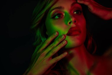 Genç, çekici bir kadın. Sarı saçlı. Parlak kırmızı ve yeşil neon ışıklarla aydınlatılmış..