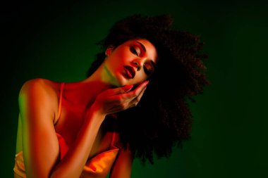 Genç bir kadının göz kamaştırıcı yakın çekimi zarafet ve güzelliği yeşil arka planda canlı ışıklandırma ve cesur stiliyle sergiliyor.