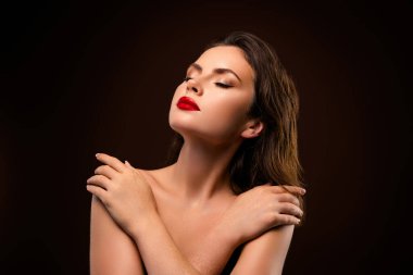 Göz alıcı kırmızı rujuyla çekici esmer bir kadın, pürüzsüz bir ten ve çarpıcı bir güzellik sergiliyor, siyah bir arkaplanda zarif bir şekilde poz veriyor.