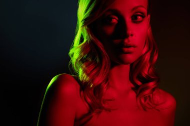 Göz kamaştırıcı genç bir kadın, neon kırmızı ve yeşil ışıklarla yıkanmış, zarafet ve güzelliği koyu bir arka plana karşı sergiliyor, moda ve tarzını ön plana çıkarıyor..