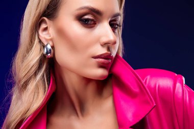 Canlı pembe bir trençkot giyen, şehvetli bir güzellik ve tarz saçan, dramatik bir mor arka plana zarif bir şekilde poz veren sarışın manken..