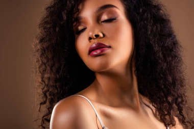 Entelektüel makyaj, zarif ifade ve şık kıvırcık saçlarla güzelliğini ve tarzını sergileyen sakin genç bir kadın.