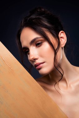 Doğal makyajı ve vurgulanmış güzelliği olan genç esmer bir kadının sanatsal tasviri zevkli ve minimalist estetik için koyu bir arka planda sunuluyor..
