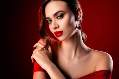 Zarif mücevherler ve sofistike makyajlar takan göz kamaştırıcı bir kadının portresi canlı kırmızı arka planda resmedilmiş. Gösterişli güzellik, lüks ve tarz.