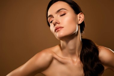 Işıl ışıl ciltli genç bir kadının dingin bir görüntüsü yumuşak bej bir arka planda sunuluyor. Güzelliği, cilt bakımını ve doğal zarafeti yakalar..