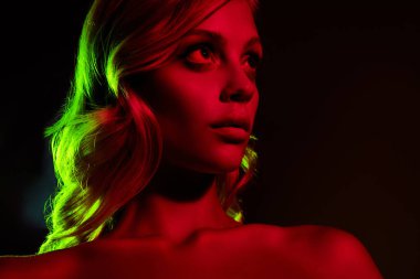 Sarı saçlı genç bir kadının zarif portresi, çarpıcı kırmızı ve yeşil ışıklarla aydınlatılmış, koyu bir arka planda moda ve güzelliği somutlaştıran.