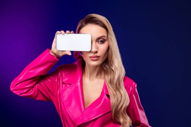 Zarif pembe elbiseli güzel sarışın kadın canlı bir arka plana karşı akıllı telefonuyla poz veriyor. Tarz, moda, güzellik ve teknoloji tasvir edilmiştir..