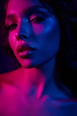 Canlı pembe ve mavi renklerle süslenmiş, neon ışıkları altında zarafet ve cazibesini ifade eden genç bir kadının dramatik bir portresi..