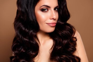 Kıvırcık saçlı, canlı makyajlı, sağlıklı ciltli, kendine güveni ve güzelliği tarafsız bir arkaplanda somutlaştıran esmer bir kadının şık fotoğrafı..