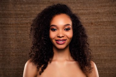 Çekici, kıvırcık saçlı, kendine güvenen, doğal güzelliğini ve zarif tarzını kahverengi desenli arka planda vurgulayan genç bir kadının yakın çekimi..