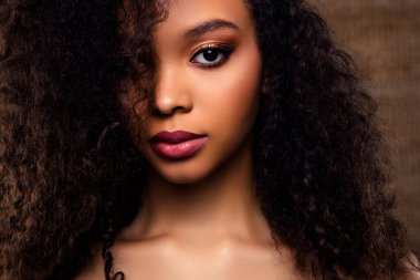 Canlı kıvırcık saçlı, çarpıcı makyajlı ve kusursuz ciltli genç bir kadının büyüleyici portresi. Görüntü, tarafsız bir zemin karşısında modern güzelliği, zarafeti ve güveni vurguluyor..