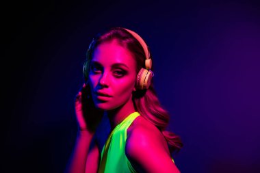 Neon pembe ve mor ışıkla aydınlatılmış, modern moda ve gece hayatı estetiğiyle aydınlatılmış, kulaklık takan moda bir kadın..