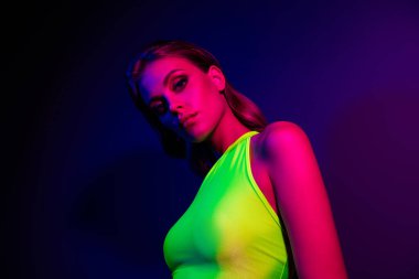 Modayı takip eden genç bir kadın, neon pembe ve mavi ışıkların altında dinamik bir şekilde poz verdi, gece hayatı ve stili etrafında modern, şık temalar için mükemmel sanatsal bir düzende moda yeşil bir kıyafet sergiliyordu..