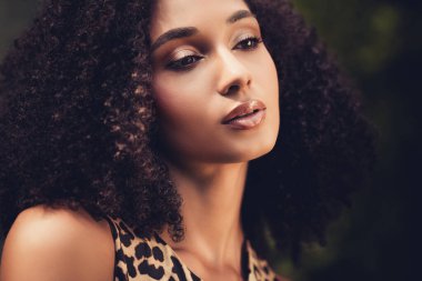 Kıvırcık saçlı, açık havada doğal ışık altında şık bir leopar desenli kıyafet sergileyen genç bir kadının çarpıcı portresi..