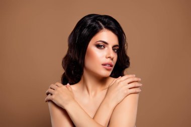 Güzel, genç, esmer, şık makyajlı ve mükemmel tenli bir kadın. Bej bir arka planda poz veriyor. Zarif ve kadınsı bir çekiciliği var..