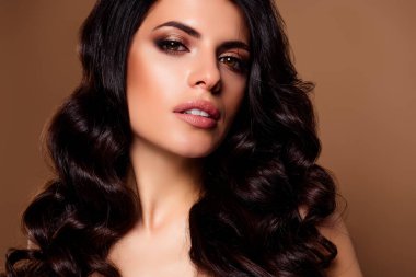 Kusursuz makyajlı ve stil sahibi genç bir esmer kadın zarif bir şekilde bej arka planda poz veriyor, zarafet, cazibe ve cazibe saçıyor..