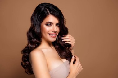 Stüdyoda genç bir esmer kadın zarif bir gülümseme ve zarif bir saç stiliyle poz veriyor, güzel ve özgüvenli bir şekilde bej bir arka plana doğru yayılıyor..