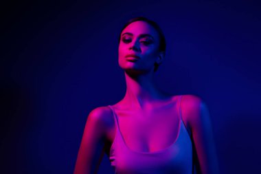 Canlı mavi ve pembe ışıklı arka planda kendine güvenen çekici bir genç kadının sanatsal portresi..