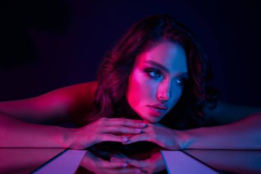 Parlak pembe ve mavi neon ışıkların altında poz veren genç esmer kadın, büyüleyici bir gece kulübünden esinlenerek güzelliği, stili, zarafeti ve modern estetiği vurguluyor..