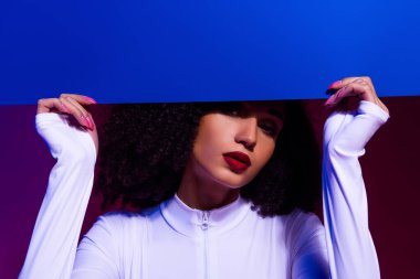 Beyaz tulumlu, canlı ultraviyole ışıkla aydınlatılmış şık bir genç kadının sanatsal portresi. Görüntü lüks, tarz ve çağdaş güzelliği çağrıştırıyor..