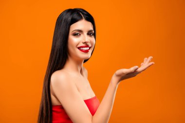 Canlı kırmızı bluzlu neşeli bir esmer kadın turuncu arka planda kendine güveni ve zarafeti var.