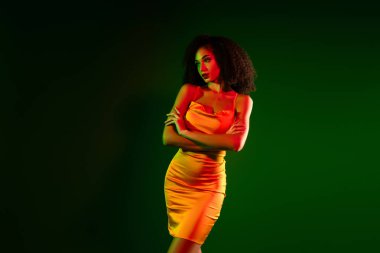 Gösterişli, sarı elbiseli şık bir kadın model canlı bir arka plana karşı duruyor. Özgüven, moda ve zarafet kavramı çarpıcı bir aydınlatma ile resmedilmiştir..