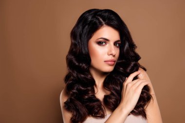 Tarz bej bir arka planda, zamansız, sofistike bir pozda, şehvetli saçları ve kusursuz makyajı olan güzel esmer bir kadının yer aldığı şık bir poz..