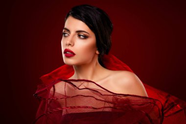 Şık görünümlü, canlı kırmızı bir kıyafet giyen zarif genç bir kadın, gradyan bir arkaplan ile görkemli bir stüdyo portresi içinde yakalandı..