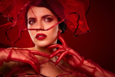 Şık esmer kadın kırmızı örgü ve göz alıcı makyajla stil yapmış, canlı, değişken bir arka plana zarifçe poz vermiş, modern moda bağlamında zarafet ve cazibeyi kapsıyor..