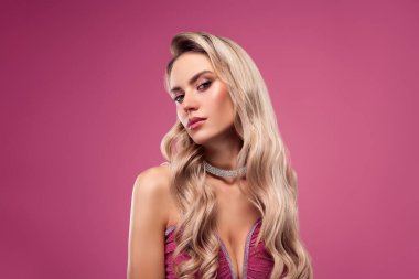 Zarif bir zarafet ve cazibe sergileyen, zarif, pembe bir elbise ve zarif mücevherler giyen güzel sarışın bir kadın. Çarpıcı pembe arka plan onun sofistike görünümünü vurguluyor, stil veya moda bağlamları için ideal..