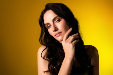 Çekici esmer kadın zarif bir pozla şık bir şekilde poz veriyor. Parlak sarı bir zemin, zarafet ve güven saçıyor..