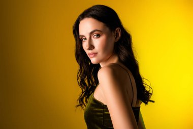 Sofistike bir kokteyl elbisesi içindeki genç esmer kadın çarpıcı sarı bir arka plana karşı poz veriyor, güzellik, kendine güven ve zarafet sergiliyor..