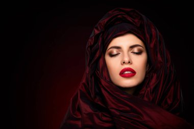 Şatafatlı kırmızı kumaşla sarmalanmış güzel bir genç kadının zarif bir yakın çekimi, coşkulu bir stil, şehvet ve çekicilik..